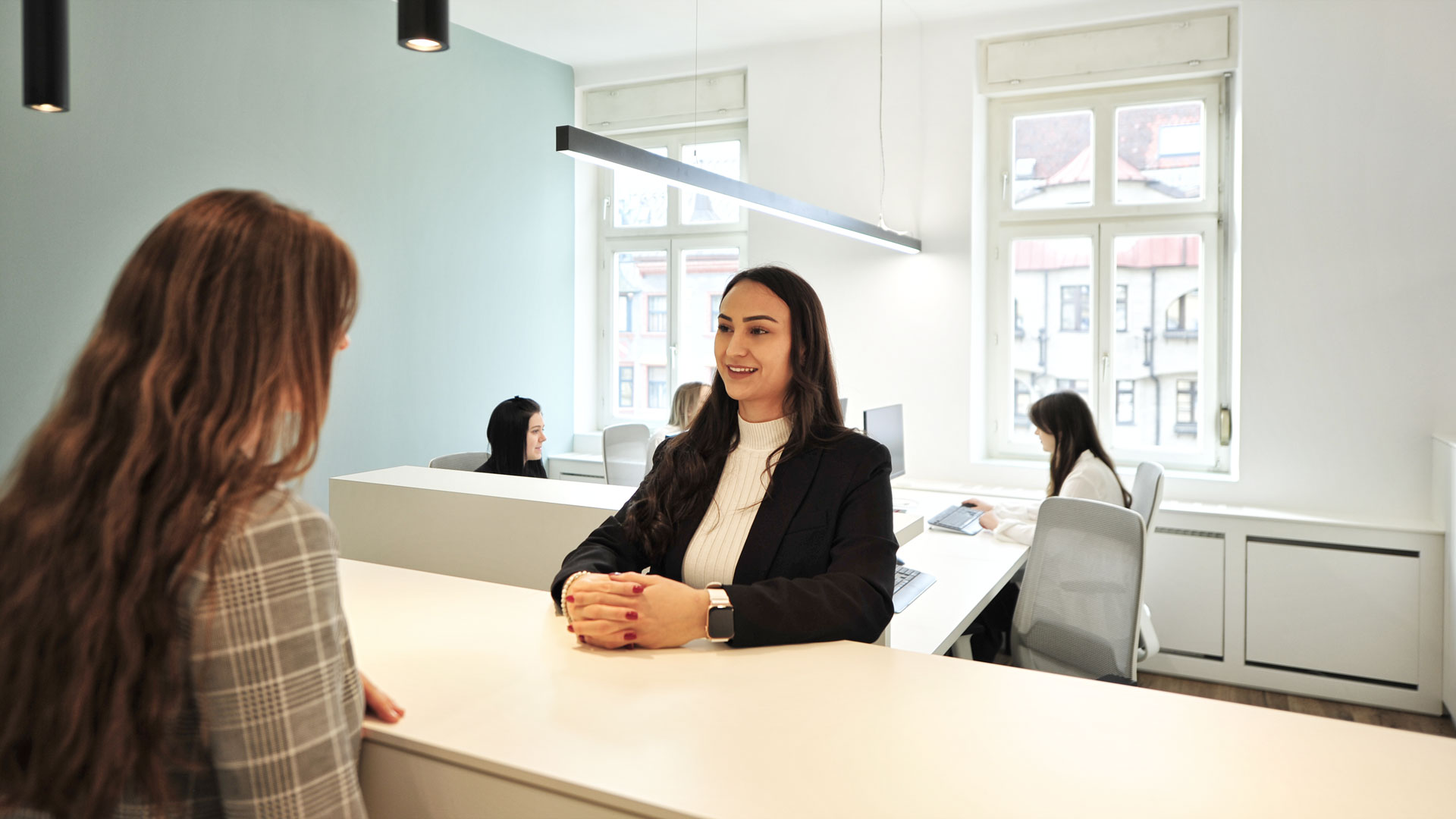 Zwei Frauen stehen sich am hellen Empfangstresen eines modernen Büros gegenüber und führen ein Gespräch.